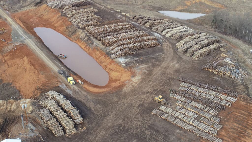 In the log yard at Eagle Lumber, located in Greensburg, KY, log trucks are unloaded, and logs are scaled. Water is pulled out of the pond and sprayed on top of the logs. The water then drains back into the pond.