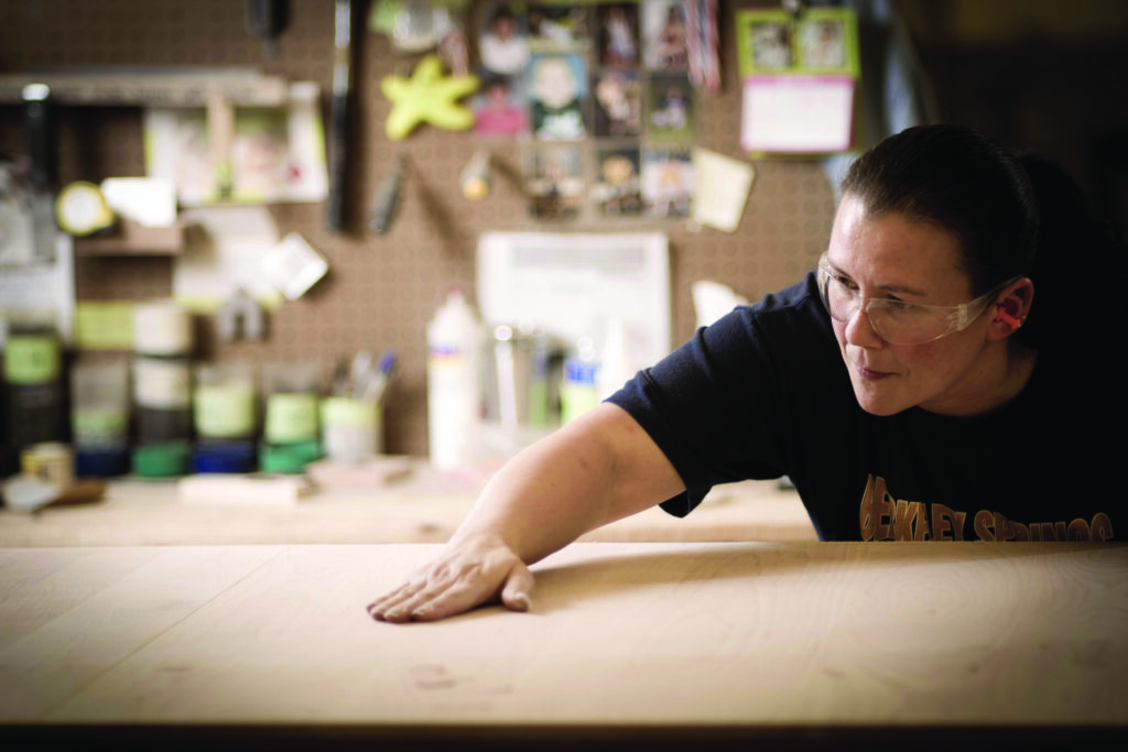 Fifty three percent of Gat Creek employees are women. Nikki Capper, a longtime woodworker, tests the smoothness of a sanded tabletop.