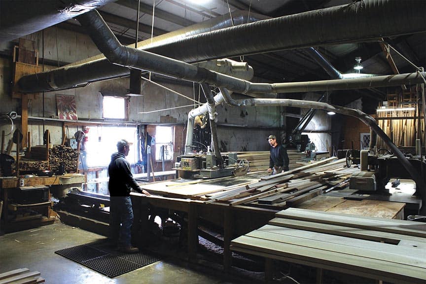 Employees at Long’s Hardwoods process lumber through a straight-line rip saw.